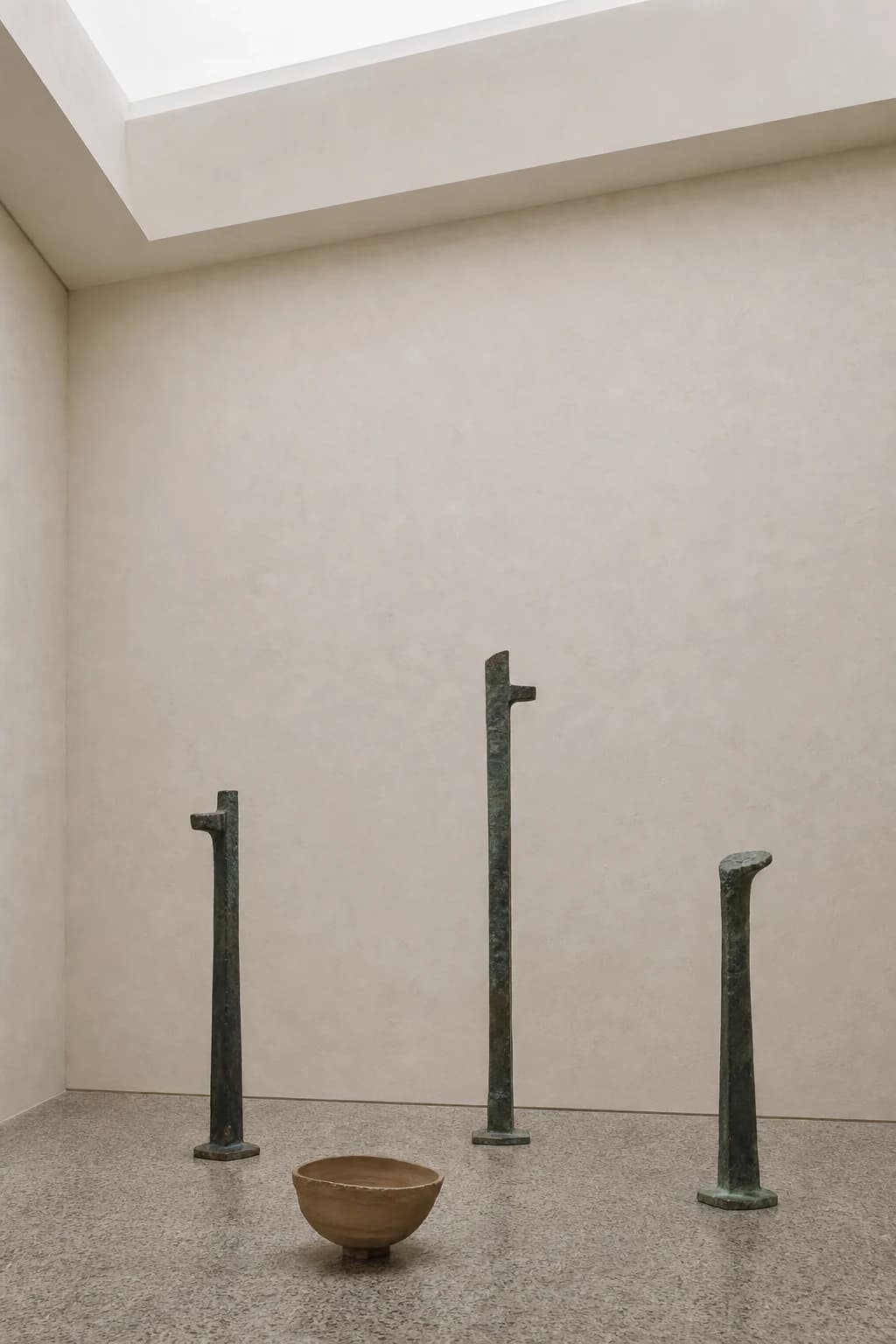 Patinated bronze forms and a clay vessel arranged in a quiet gallery